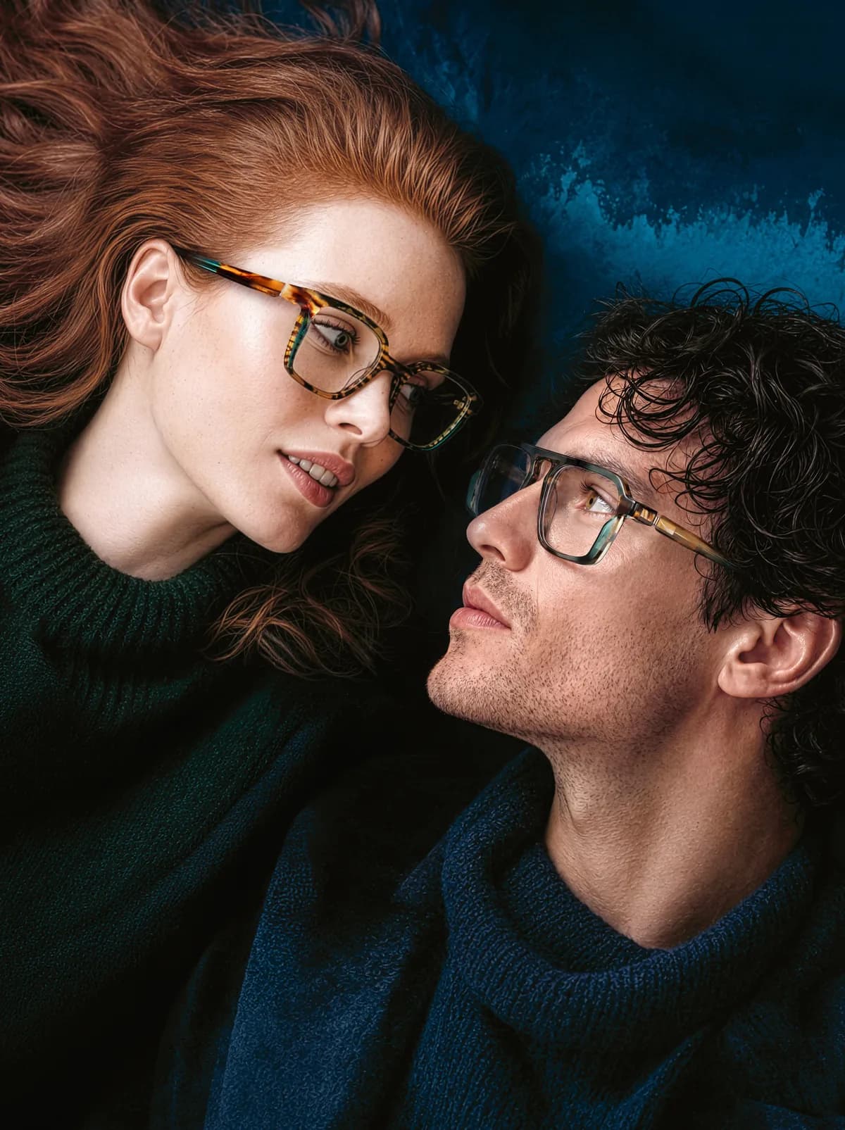 Two people wearing J.F. Rey optical frames, facing one another against a deep blue background