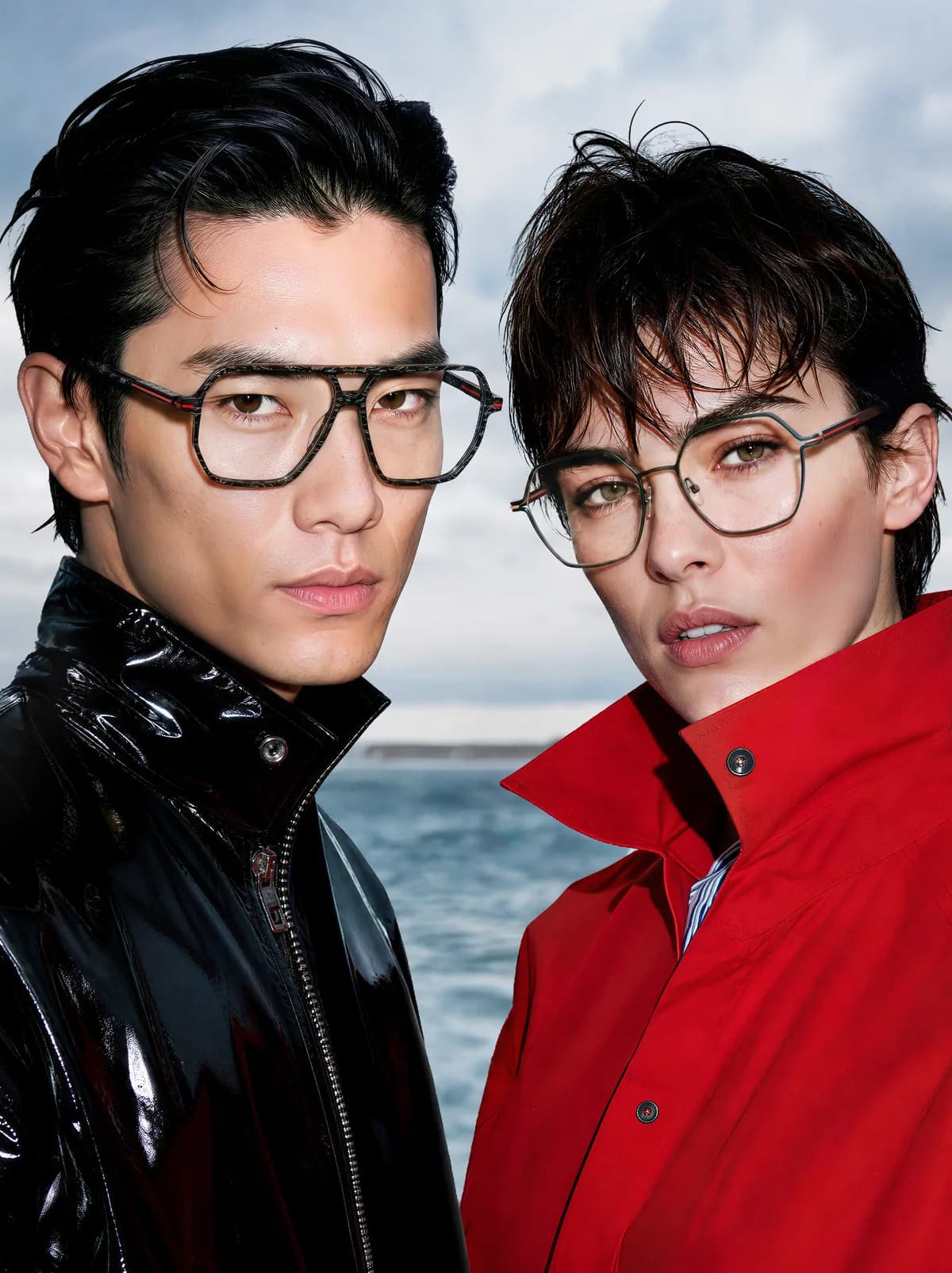 Two people wearing angular J.F. Rey optical frames, in black and red outerwear beside the sea
