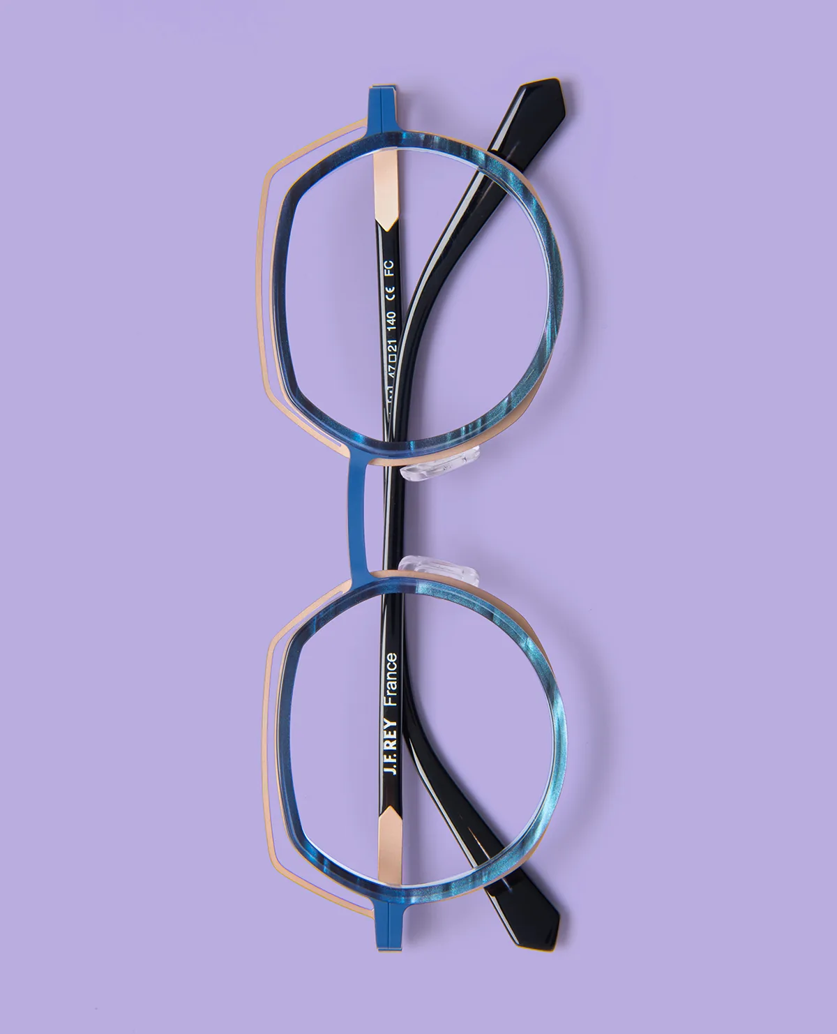 Blue-toned J.F. Rey JF3161 with a warm metallic-colored upper outline, photographed vertically on lilac