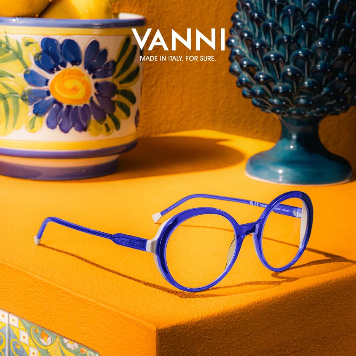 Round blue VANNI optical frame on a yellow surface with painted ceramics and lemons