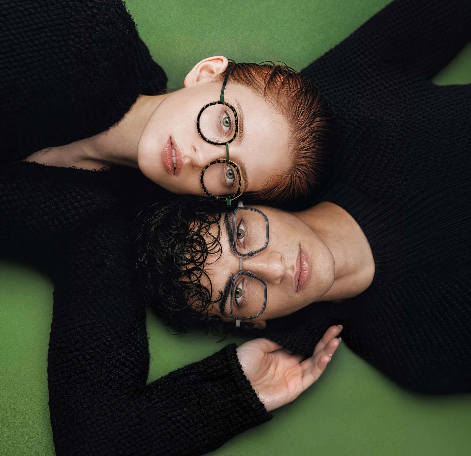 Two adults reclining on a green background wearing J.F. Rey optical frames